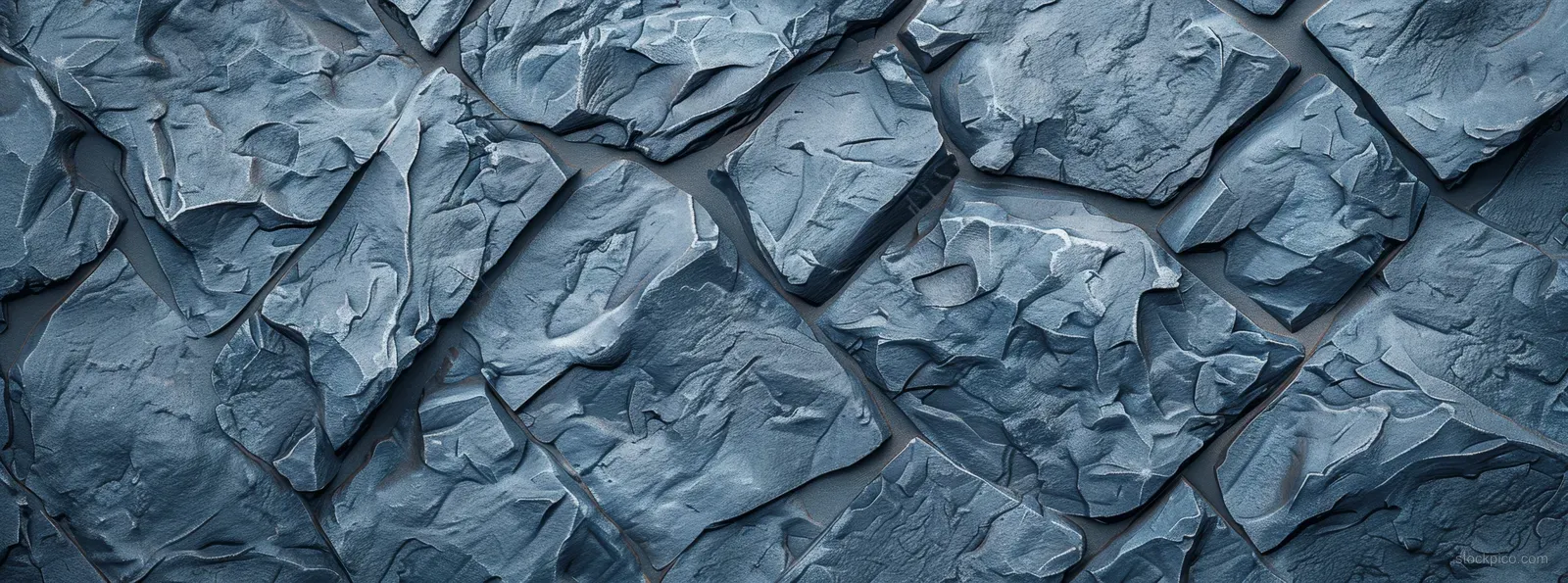 Close-up of blue-grey basalt rock wall texture with rough cracks and uneven stone blocks.