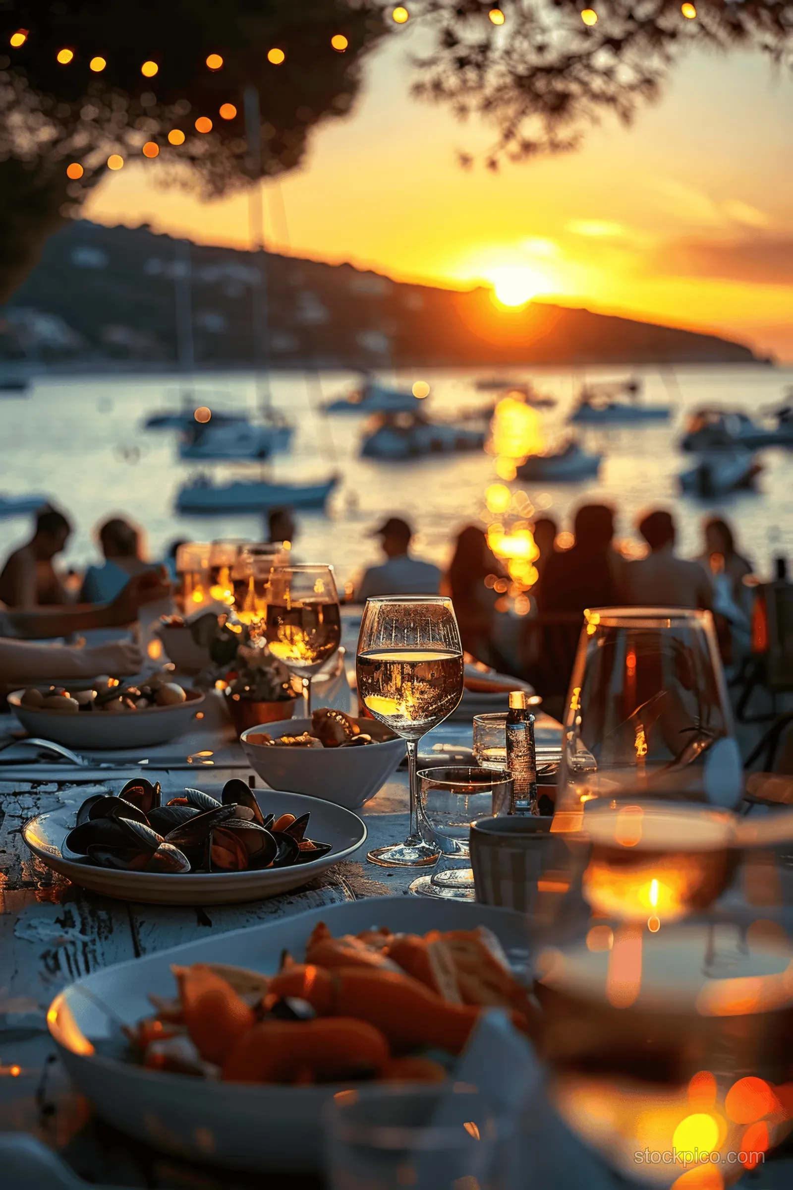 Sunset dinner table with mussels and wine glasses overlooking a harbor of boats and the sea.