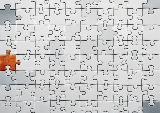 White jigsaw puzzle pieces on a tabletop with one brown missing piece creating a gap