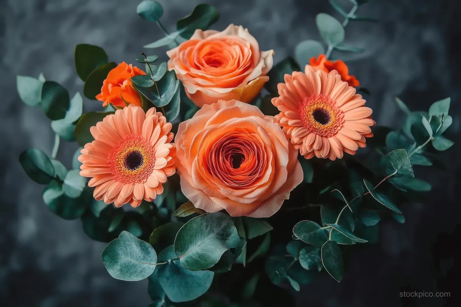 Peach roses and orange gerbera daisies with eucalyptus leaves arranged in a bouquet against a dark textured background.