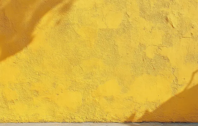 Bright yellow textured wall with uneven paint and soft sunlight shadows on its rough surface.