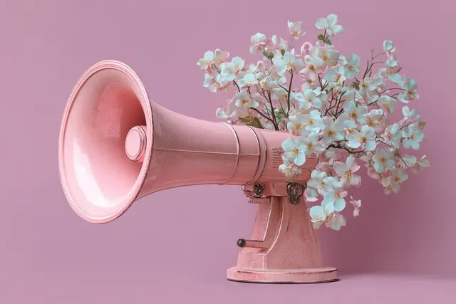 Vintage pink megaphone with white and pink flowers blooming from its back on a soft pink background.