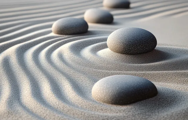 Smooth river stones resting on raked sand, forming concentric wave patterns in soft light