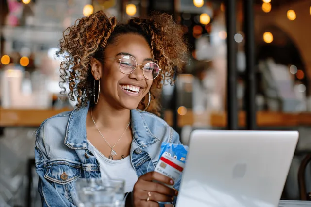 Laughing woman with laptop and credit card in cafe