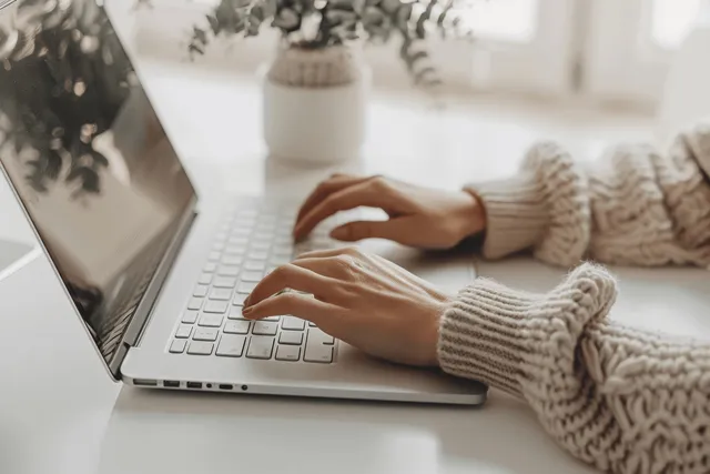 Woman’s hands typing on laptop keyboard in bright office desk workspace