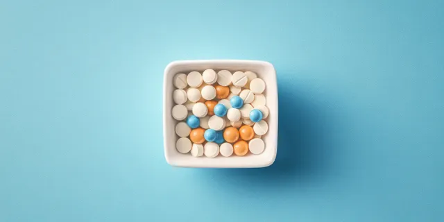 Top view of assorted colorful pills in a white square dish on blue textured background