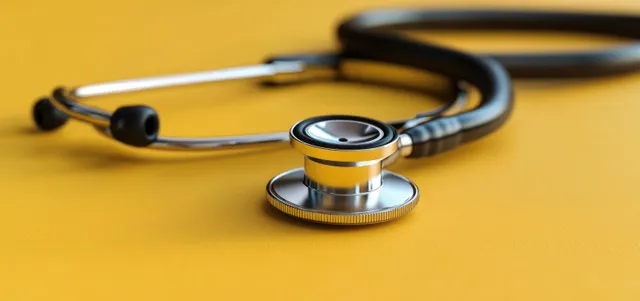Silver stethoscope with black tubing lying on a bright yellow surface for a medical diagnosis theme.