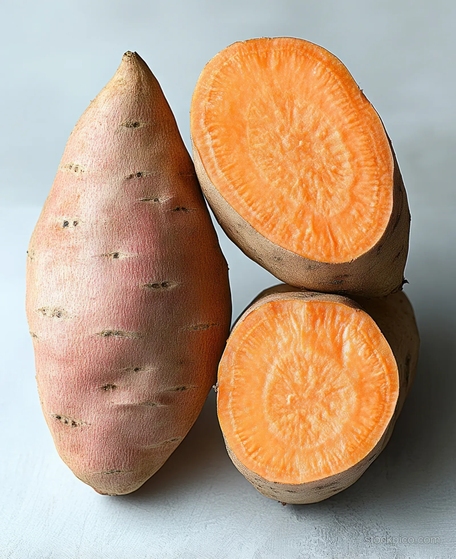Whole and halved sweet potatoes with rough skin and bright orange flesh on a light surface.