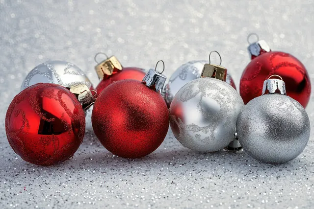 Red and silver Christmas ornaments rest on sparkling snow with glittery highlights and soft blurred light.