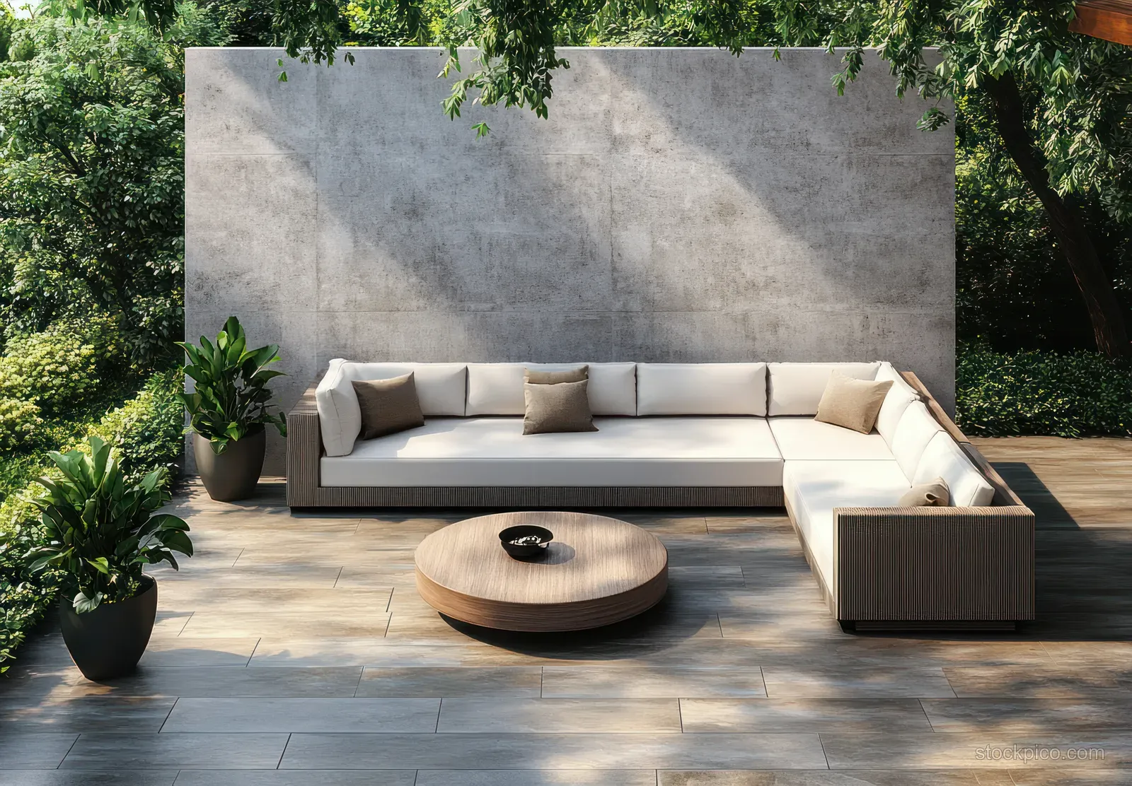 Minimalist outdoor lounge with beige sofa against a concrete wall, round wood table, potted plants, and soft sunlight shadows.