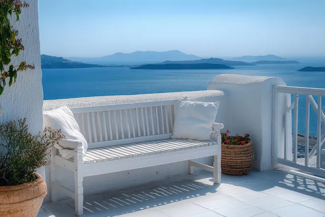 White cushioned bench on a sunny terrace overlooks calm blue sea and distant islands under clear sky.
