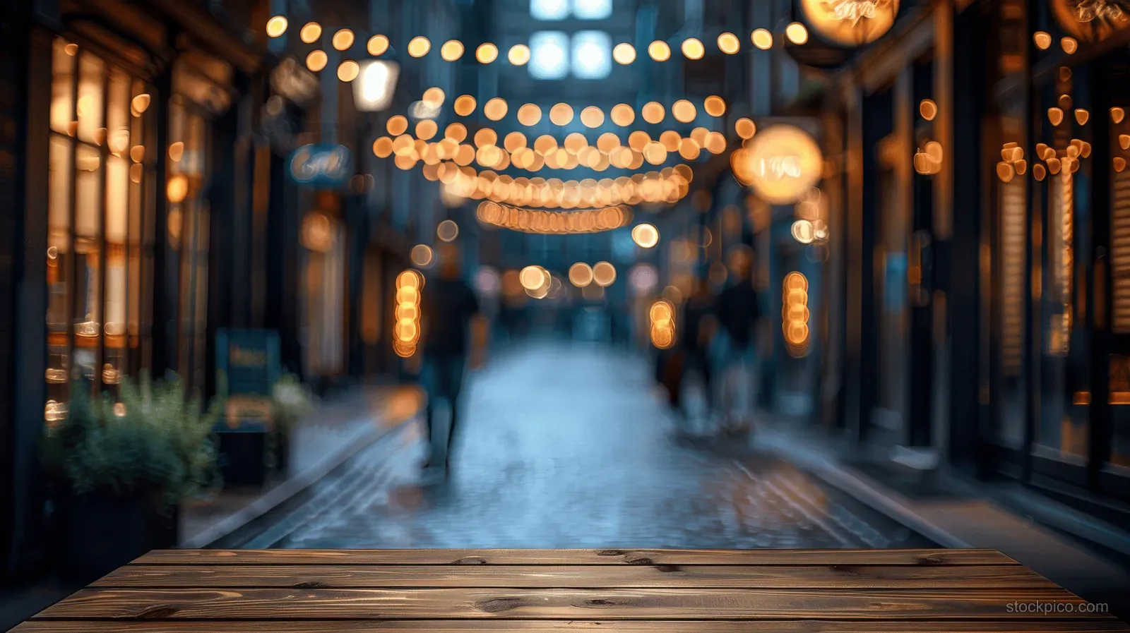 Empty wooden table top in the foreground with blurred warm Christmas fair lights on a night market street.