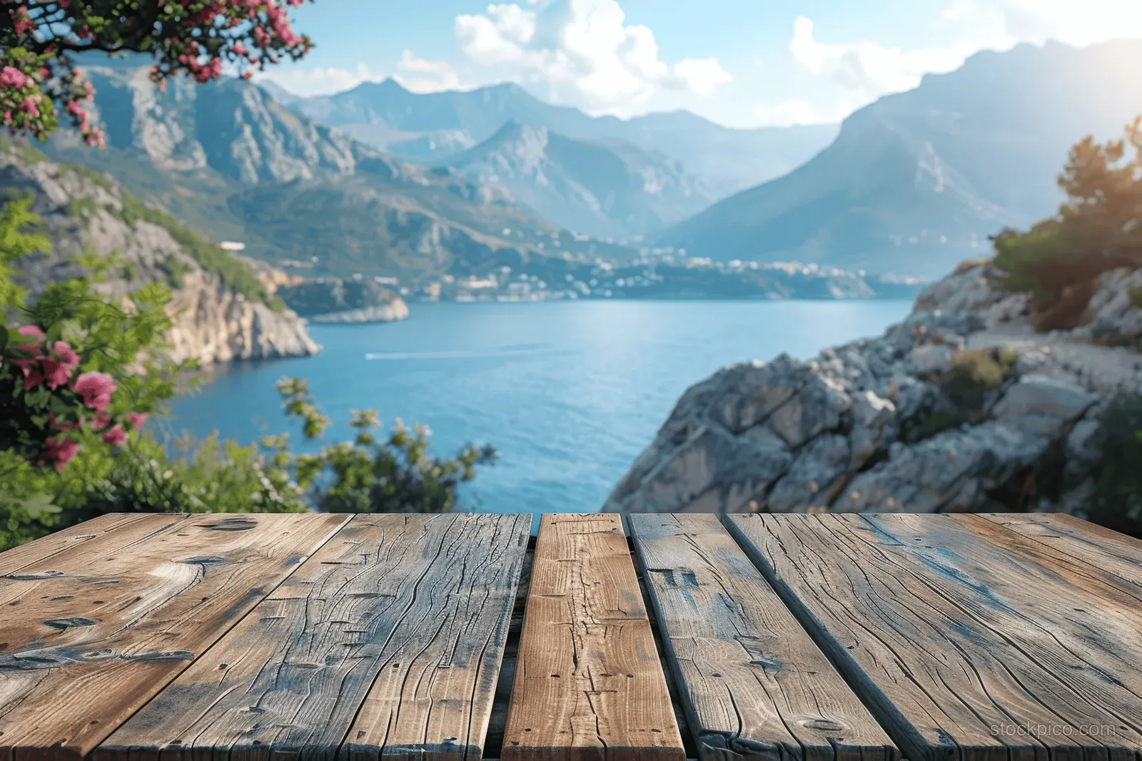 Rustic wooden table in the foreground overlooking a coastal mountain sea view with blooming flowers and clear sky.