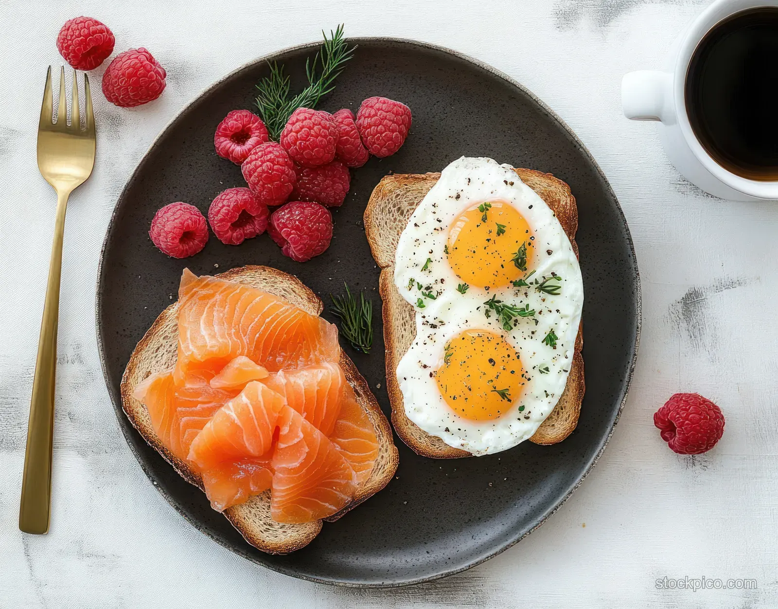 Breakfast plate with smoked salmon, toast, sunny-side eggs, herbs, raspberries, and a cup of black coffee.