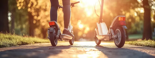 Two electric scooters on sunlit park path with riders’ legs and warm backlight