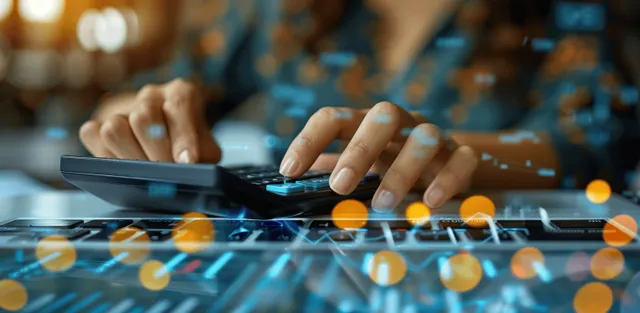 A businesswoman is budgeting with a calculator and laptop at her office desk.