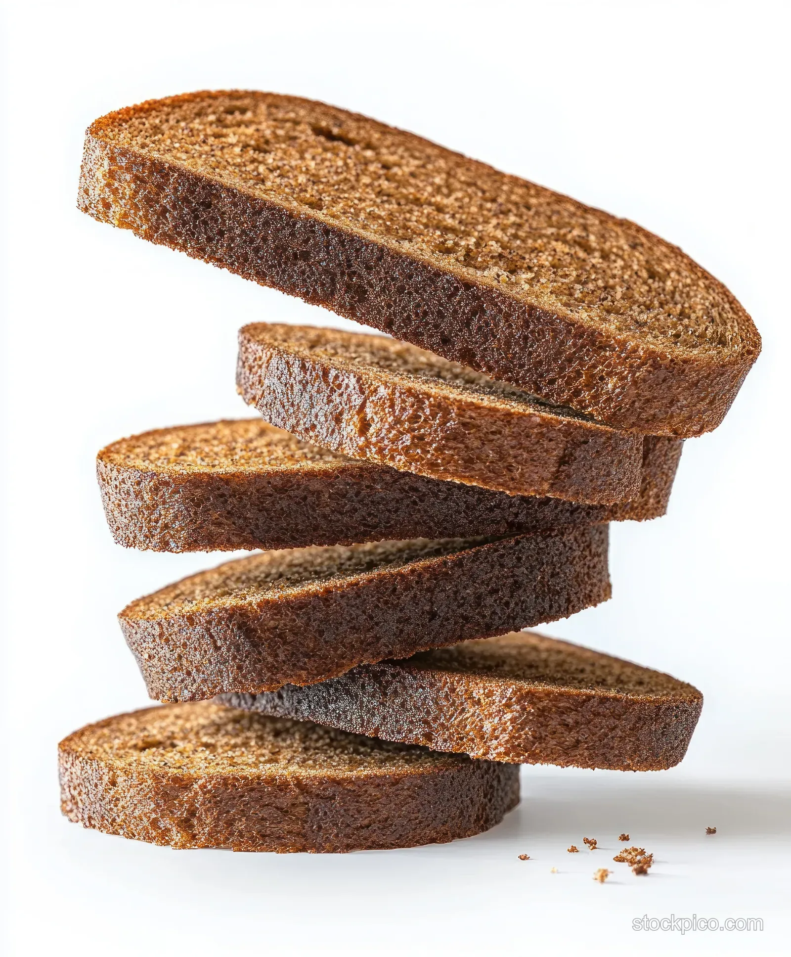 Five whole grain brown bread slices stacked in a spiral arrangement on a white background with scattered crumbs.