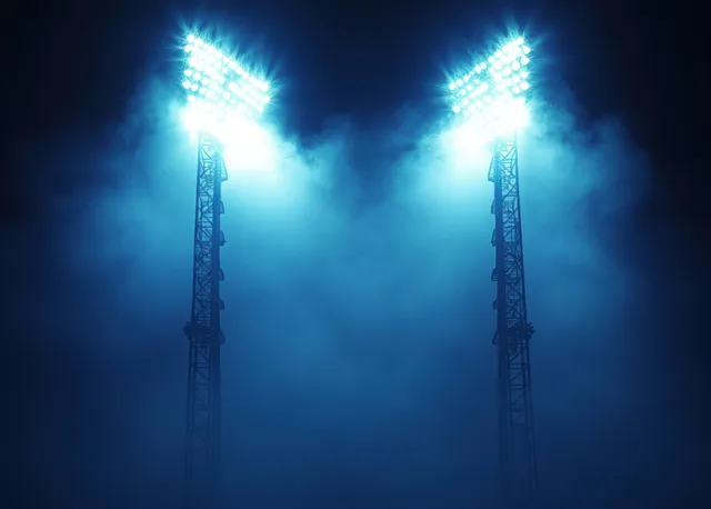 Illuminated stadium floodlights pierce foggy night sky, creating dramatic beams and open space