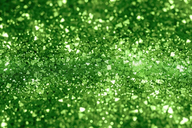 Close-up green glitter particles sparkling with light reflections across a textured surface