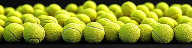 Rows of yellow-green tennis balls sit on a textured court surface with dramatic side shadows.