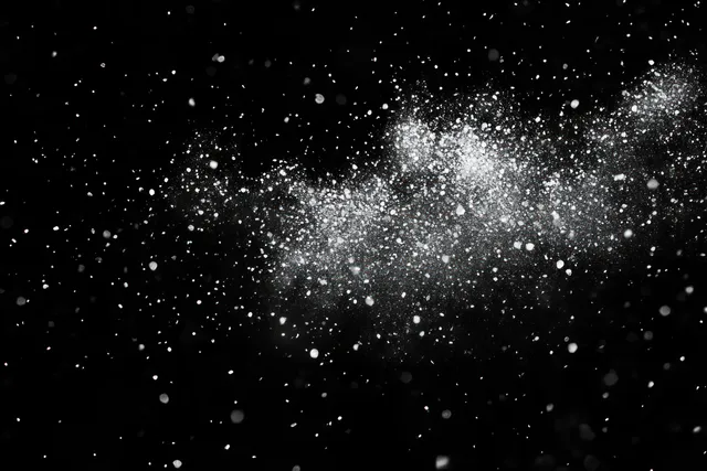 White powder particles scatter and float through the air against a dark black background.