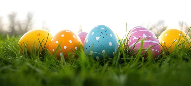 Colorful Easter eggs with polka dots and patterns lying in green grass under bright outdoor light.