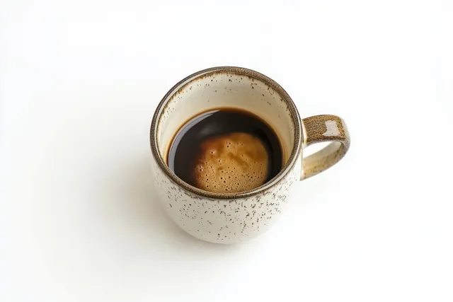 Overhead view of black coffee with crema in a speckled ceramic mug on a white background.