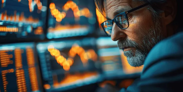 A financial analyst leans toward multiple monitors displaying glowing stock charts and market indicators in a dark office.