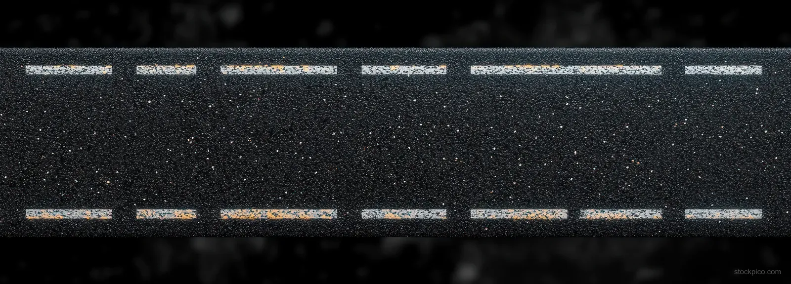 Aerial view of asphalt road surface with white dashed lane markings and worn orange paint over rough gravel texture.