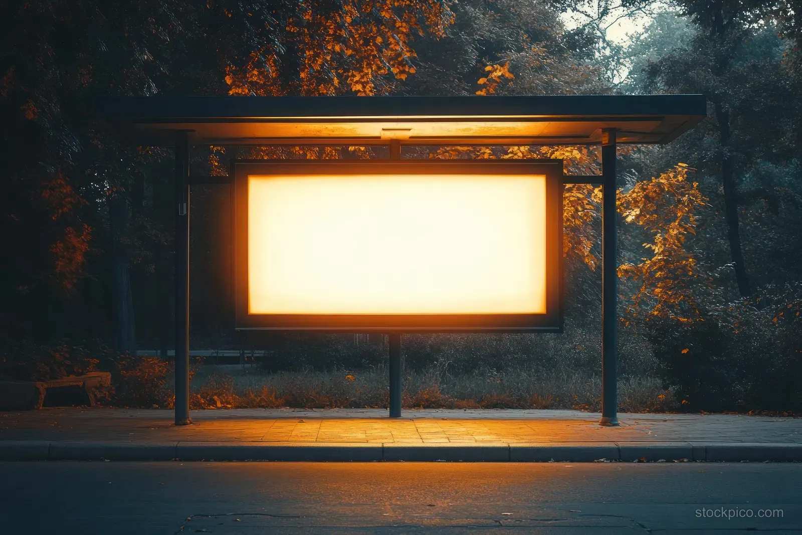 An empty illuminated advertising billboard on a city bus stop shelter at dusk.