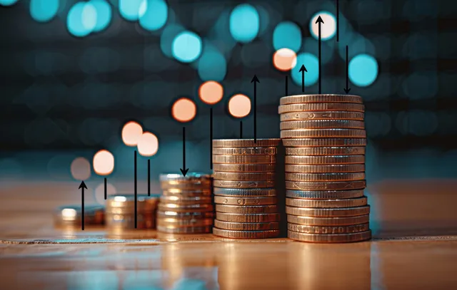 Gold coins stacked beside glowing up-arrow chart over a blurred financial background.