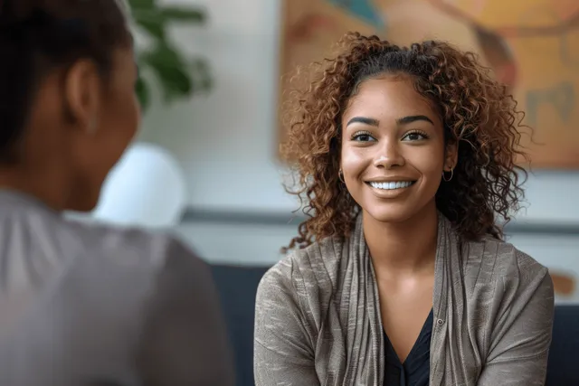 Smiling young woman with curly hair sitting indoors during a friendly conversation