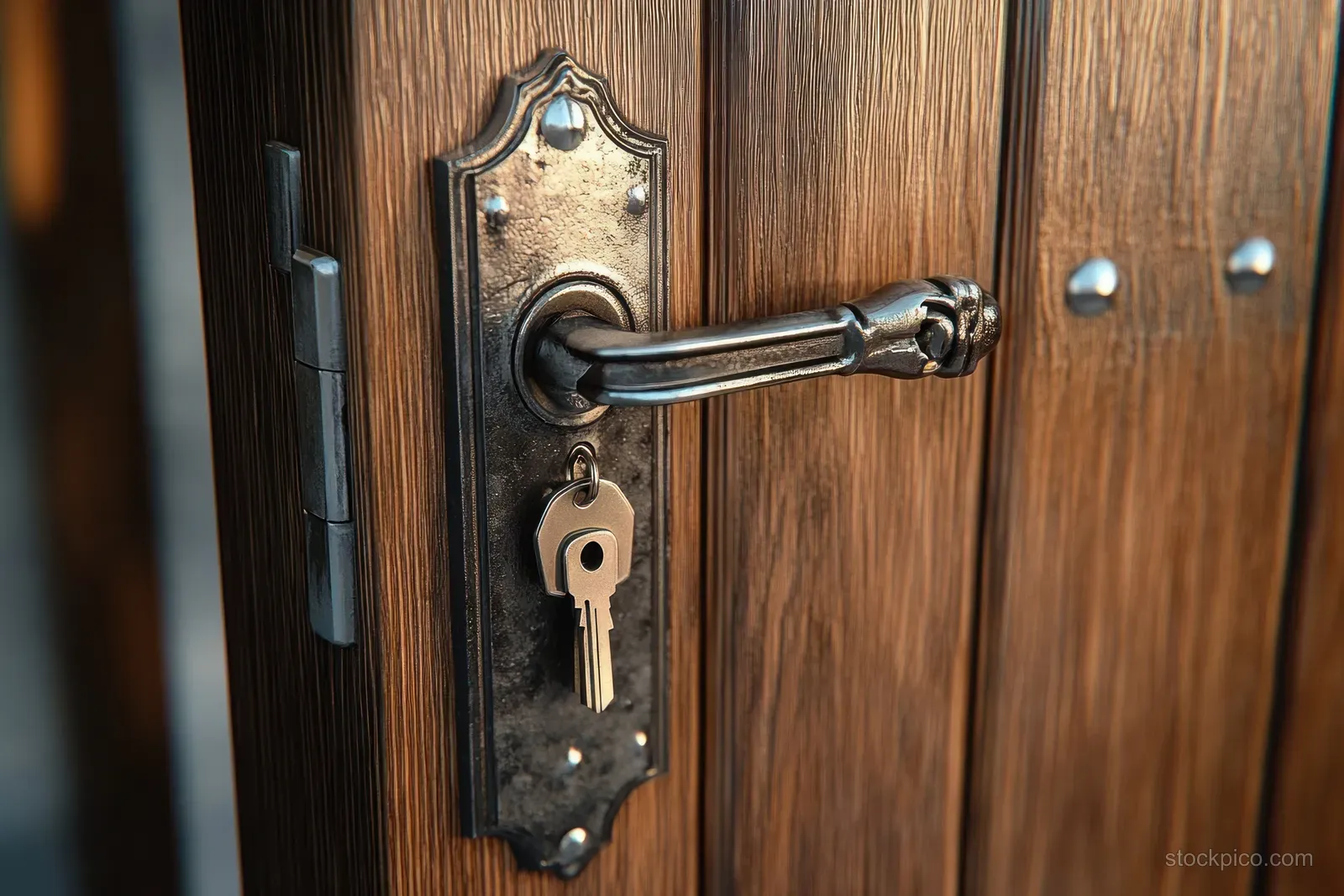 Ornate antique door handle with a key inserted in the lock plate on a weathered wooden door.