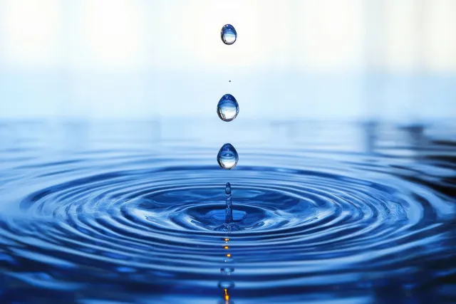 Three water droplets fall into a blue pool, forming concentric ripples across the surface.