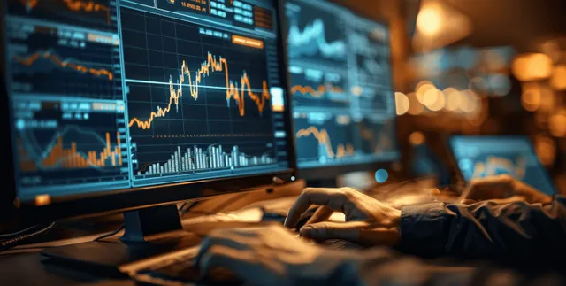 Analyst’s hand adjusts glowing stock chart indicators on a multi-monitor trading desk in a dim office.