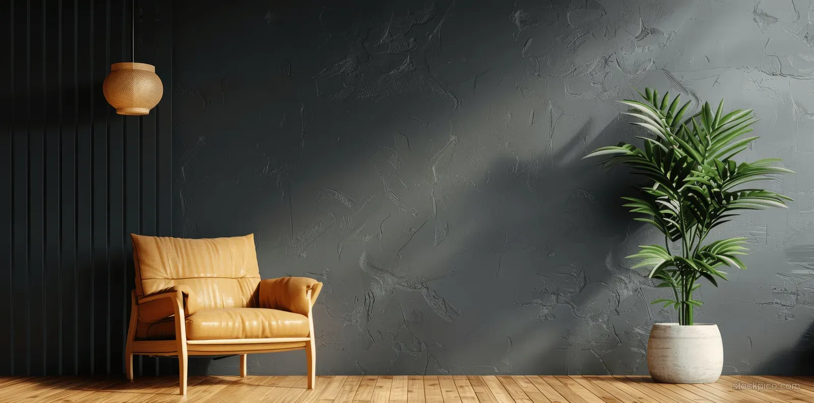 Tan leather armchair sits on a wooden floor beside a dark gray wall with a pendant lamp and potted plant.