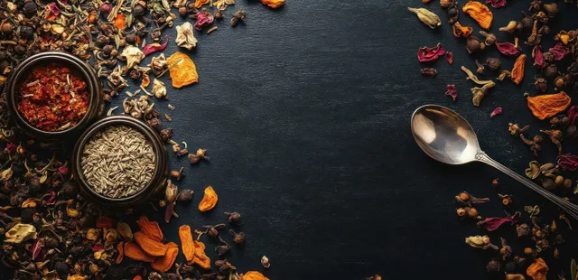 Top view of two spice jars with dried flower petals and a spoon on a dark textured surface.