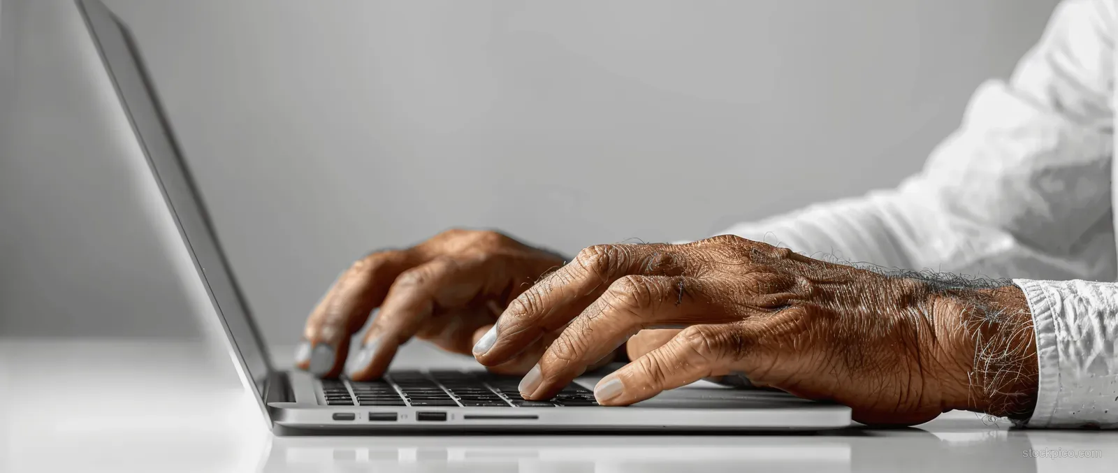 Closeup of hands typing on a laptop while using a smartphone on a modern office desk with a clean white background.