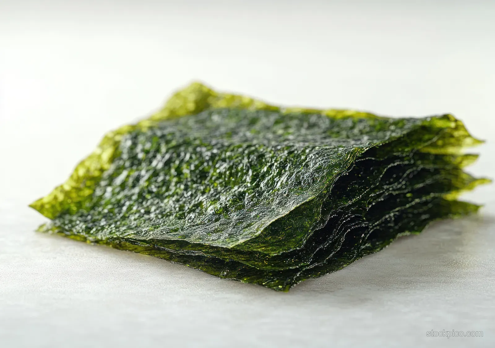 Stacked dark green roasted seaweed sheets lie on a pale surface, showing crisp layered texture.