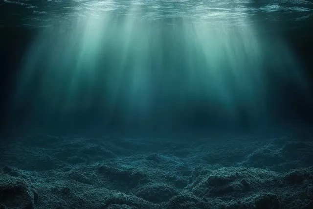 Sunlight rays penetrate clear ocean water, illuminating a textured seabed with blue haze.
