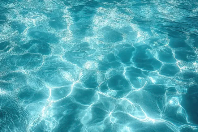 Clear turquoise water shows gentle ripples and shimmering sunlight reflections forming abstract wave patterns.