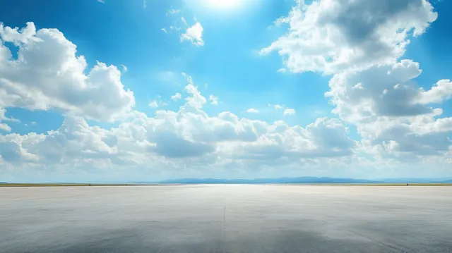An empty asphalt road stretches to the horizon beneath a bright blue sky with fluffy white clouds.