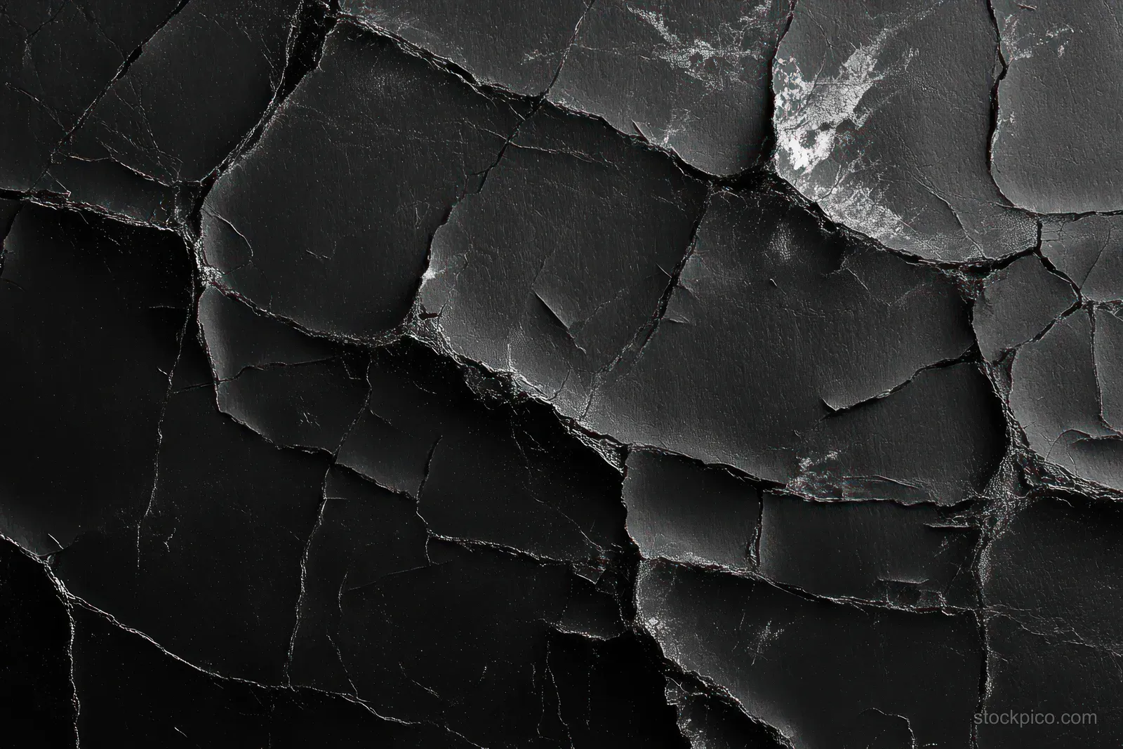 Close-up of a cracked black surface with peeling layers and irregular fracture lines.