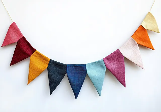 Colorful triangular fabric pennant flags hang from a string in an arc against a white background.