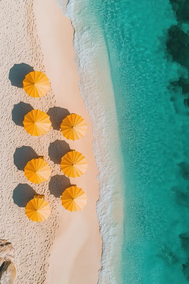 Aerial view shows nine yellow beach umbrellas on sand with turquoise water beside them.