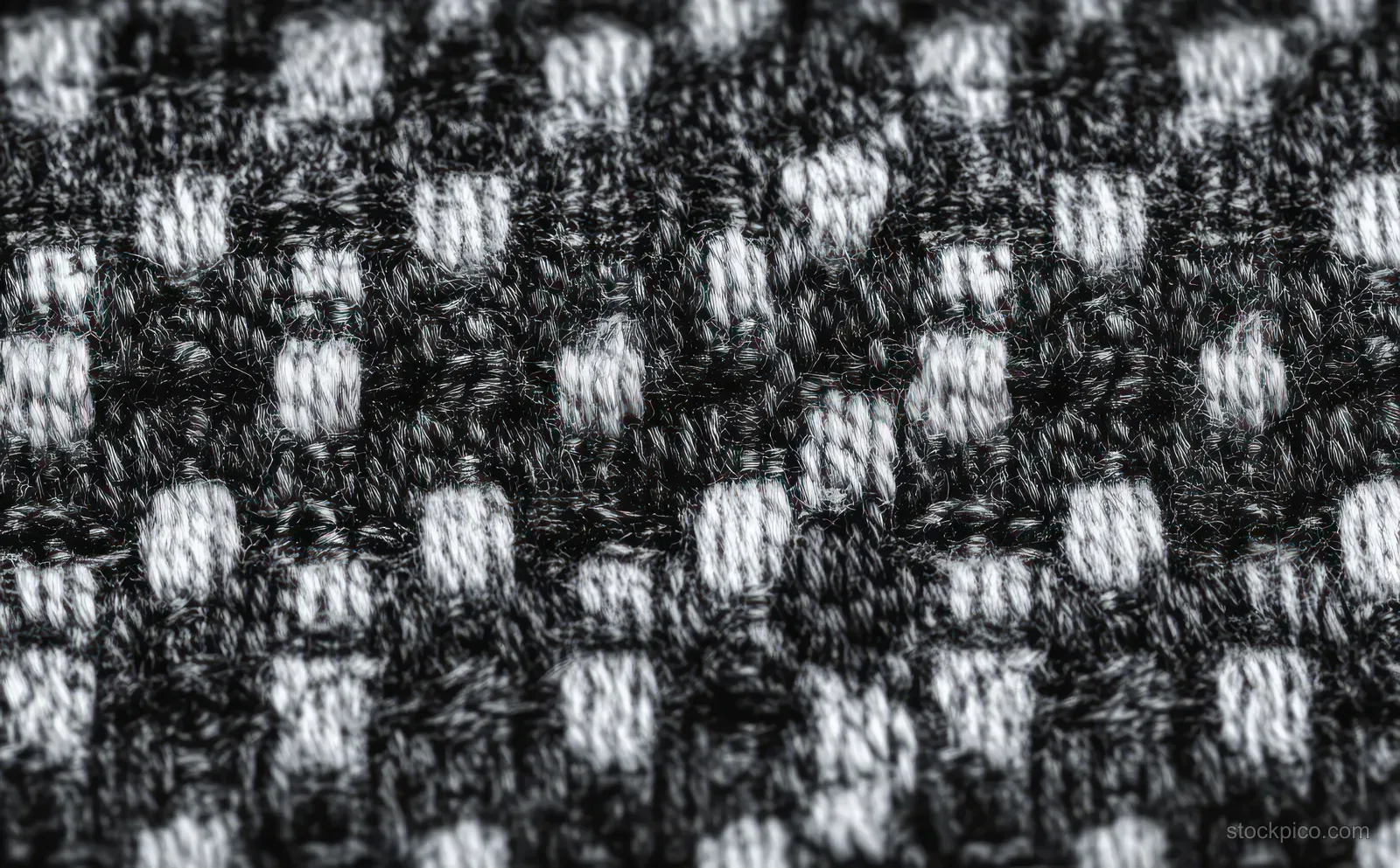 Macro close-up of black and gray woven fabric with interlaced yarn strands forming a rectangular check pattern.