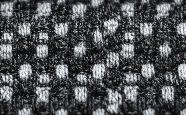 Macro close-up of black and gray woven fabric with interlaced yarn strands forming a rectangular check pattern.