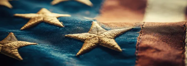 An American flag waves softly in focus blur, highlighting blue field stars and textured fabric.
