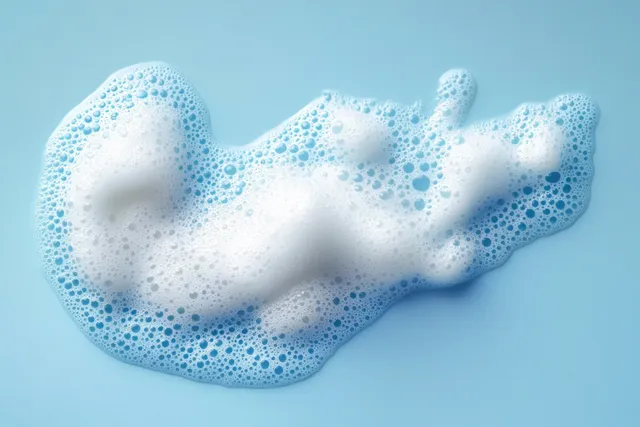 White soap foam curls with dense bubbles on a pastel blue background.