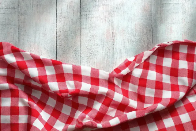 Red and white gingham fabric draped on weathered wooden table, soft folds